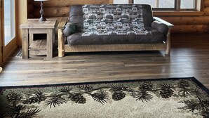Een blokhutinterieur met een leren bank, een kleine tafel met een lamp en een groot raam.