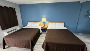 A hotel room with two single beds, a nightstand with a lamp, a window with curtains, and a wall-mounted heater. - Budget Inn (Thomasville)