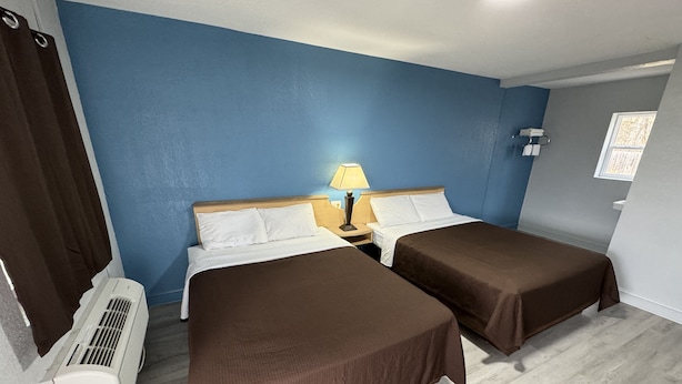 A room with two beds, a nightstand with a lamp, a window, and an air conditioning unit. - Budget Inn (Thomasville)