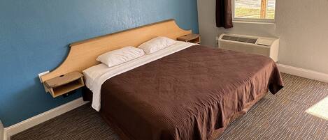 Una cama bien tendida con colcha marrón y almohadas blancas, cabecera de madera y una mesita de noche.