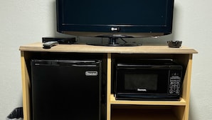 A wooden entertainment center with a flat-screen TV, a Kenmore microwave, and a Magic Chef refrigerator. - Budget Inn (Thomasville)