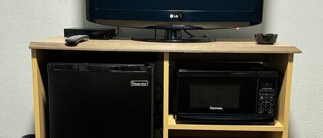 A wooden entertainment center with a flat-screen TV, a Kenmore microwave, and a Magic Chef refrigerator.