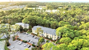 Ein Hotel mit Parkplatz, umgeben von dichter Vegetation und einem Gewässer im Hintergrund, aus der Vogelperspektive.