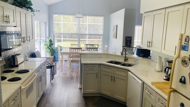 A modern kitchen with white cabinets, a built-in oven, a sink, and a dining area with chairs and a table. - Oakchase villa with pool and gameroom sleeps 8 guests easy!  (Davenport)