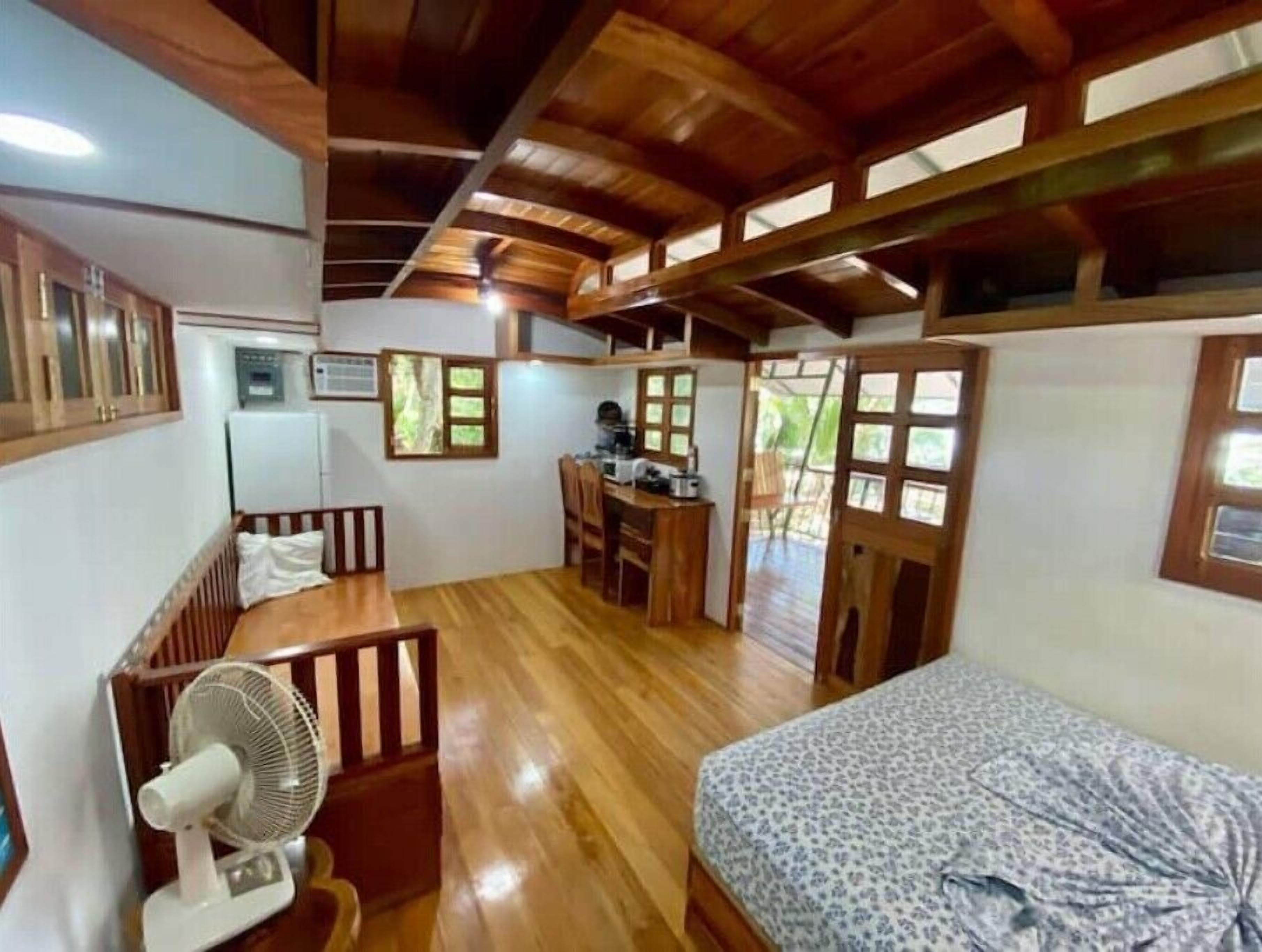 Ein kleines Zimmer mit Bett, Schreibtisch und Ventilator.