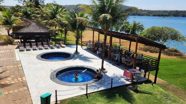 A pool area with two hot tubs, a covered seating area, and a view of a lake. - Aldeia do Lago 306H (Caldas Novas)