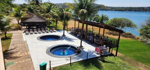 A pool area with two hot tubs, a covered seating area, and a view of a lake. - Aldeia do Lago 306H (Caldas Novas)
