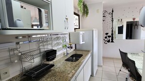 A modern kitchen with a granite countertop, built-in appliances, and a hanging wine rack. - Aldeia do Lago 306H (Caldas Novas)