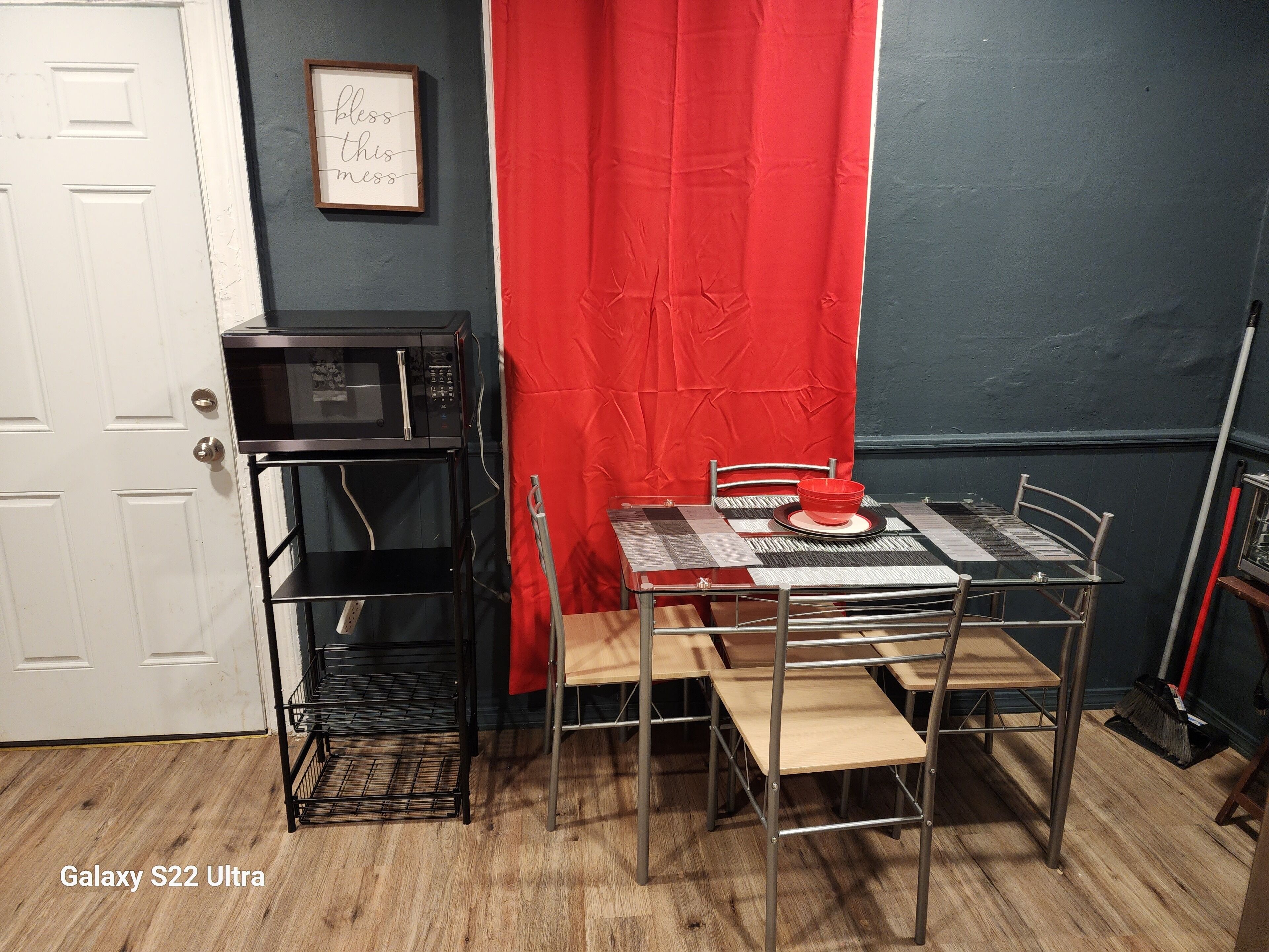 A compact kitchen with a microwave, a metal table with chairs, and a red curtain.