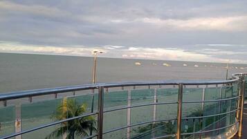 A coastal view from a balcony with a glass railing overlooking the sea, palm trees, and a sandy beach.