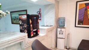 A reception area with a marble counter, a coffee machine, a water dispenser, and a framed artwork on the wall. - Manaira Flat (João Pessoa)