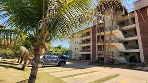 Un edificio de varios pisos con balcones, zona de estacionamiento y palmeras.