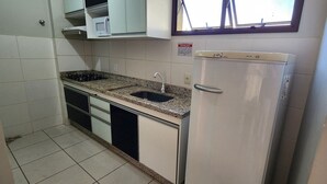Una cocina compacta con armarios blancos, encimera de granito, pileta de acero inoxidable y refrigerador blanco.