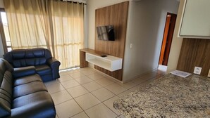 Una sala de estar con un sofá de cuero negro, un televisor de pantalla plana montado en una pared de madera, una consola blanca y suelo de baldosas.