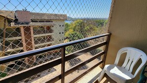 Un balcón con una barandilla de malla, una silla de plástico blanco y vistas a un edificio con tejado de tejas.