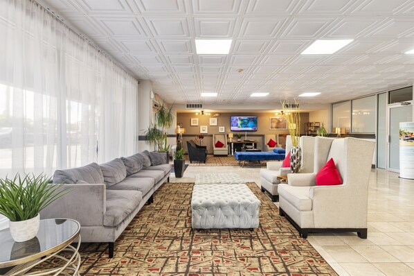 A modern lobby with a grey sofa, a white armchair, a patterned rug, and a television on the wall.