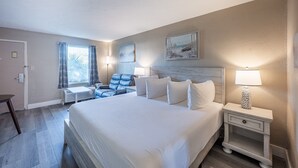Una habitació d'hotel amb un llit gran, un escriptori, una cadira i una tauleta de nit amb una làmpada.