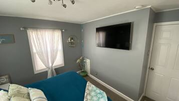 Un dormitorio con cama, televisor montado en la pared, ventana con cortinas y una puerta.