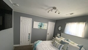 Une chambre à coucher avec un lit, une porte, un miroir fixé au mur et un luminaire au plafond.