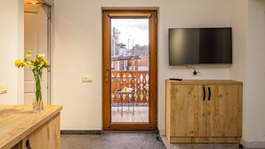 A room with a wooden door leading to an outdoor area, a flat-screen TV mounted on the wall, and a wooden cabinet. - Taniqinn Dilijan Hotel (Dilijan)