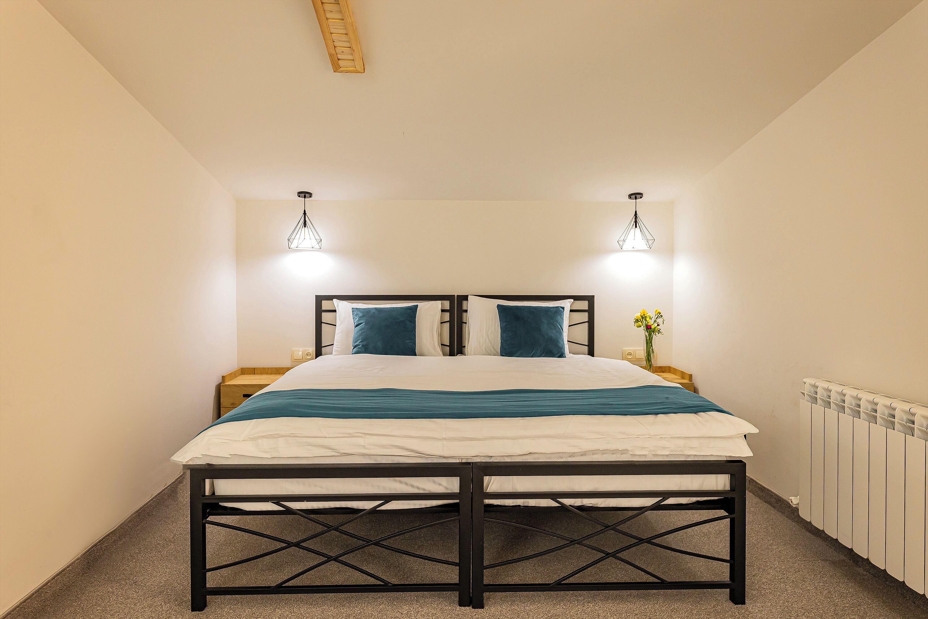A bedroom with a bed, two bedside tables, a radiator, and a hanging light fixture.