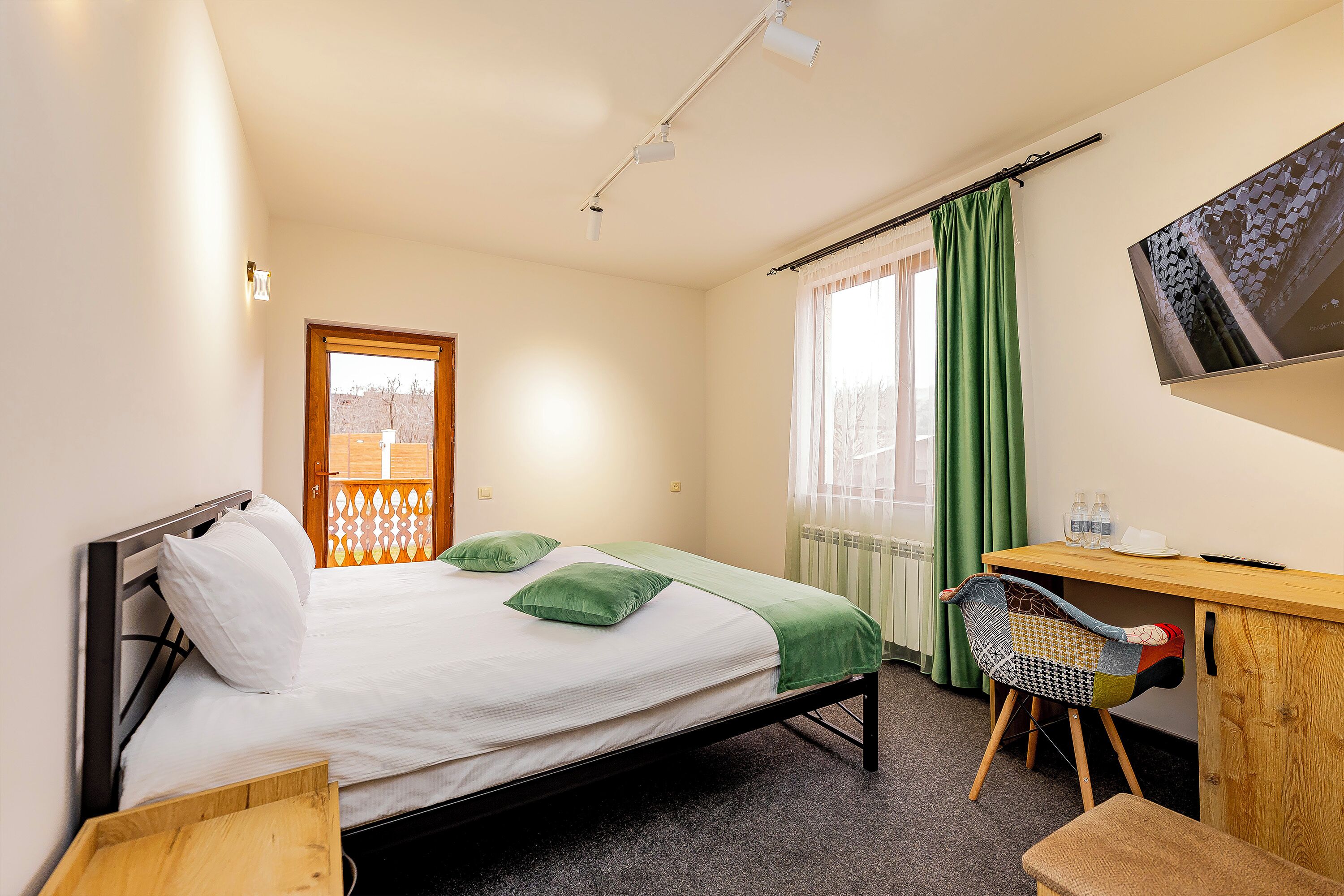 Una habitación de hotel con cama, escritorio con silla, televisión y ventana con cortinas.