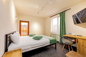 Una habitación de hotel con cama, escritorio con silla, televisión y ventana con cortinas.