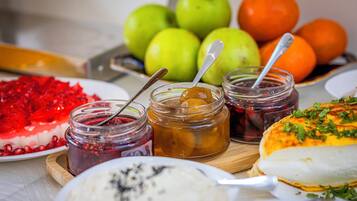 Una mesa con diferentes alimentos, entre ellos frutas, mermeladas y un postre.