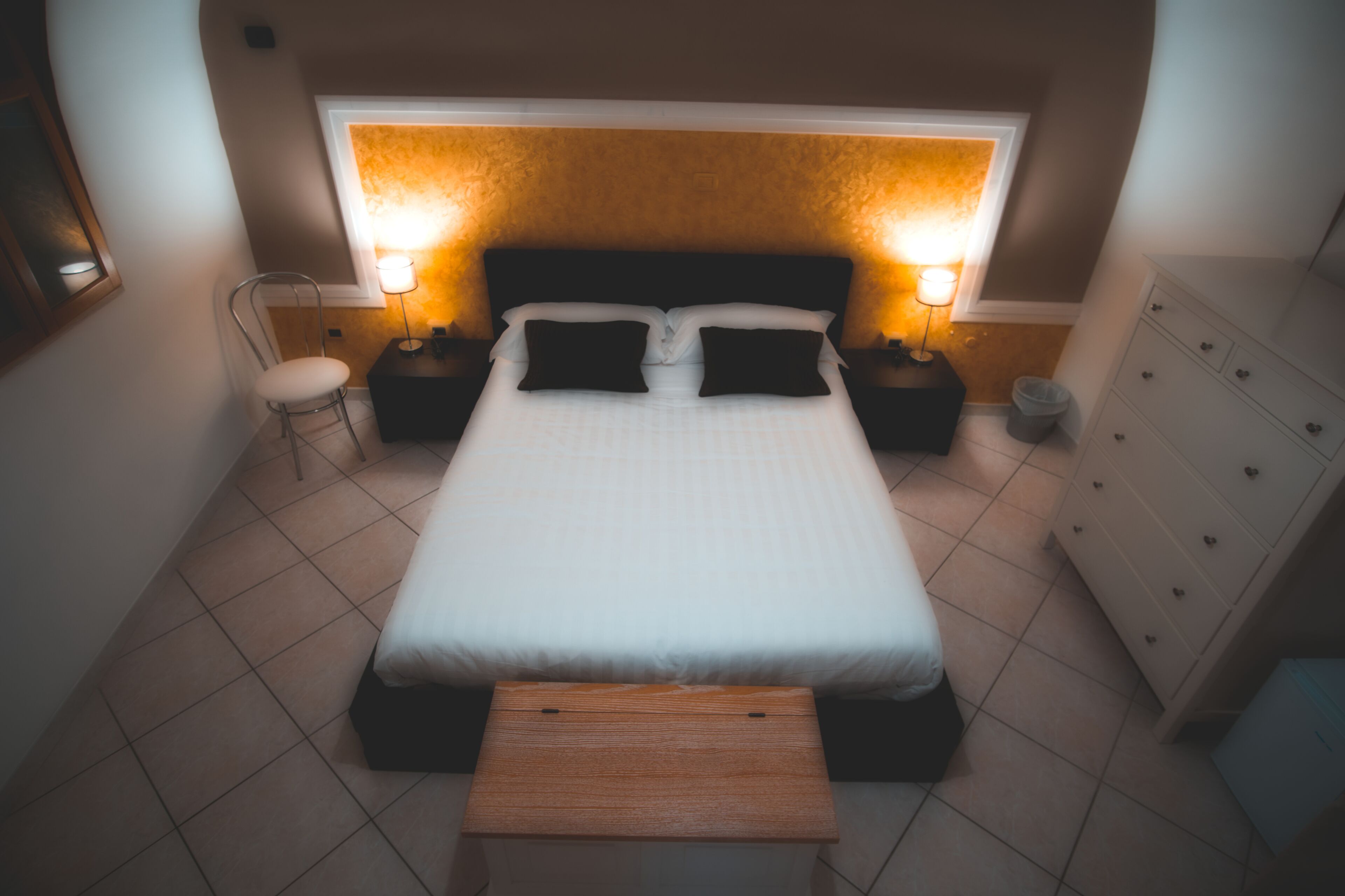 Una camera da letto ordinata con un letto, comodini, una sedia e una cassettiera.