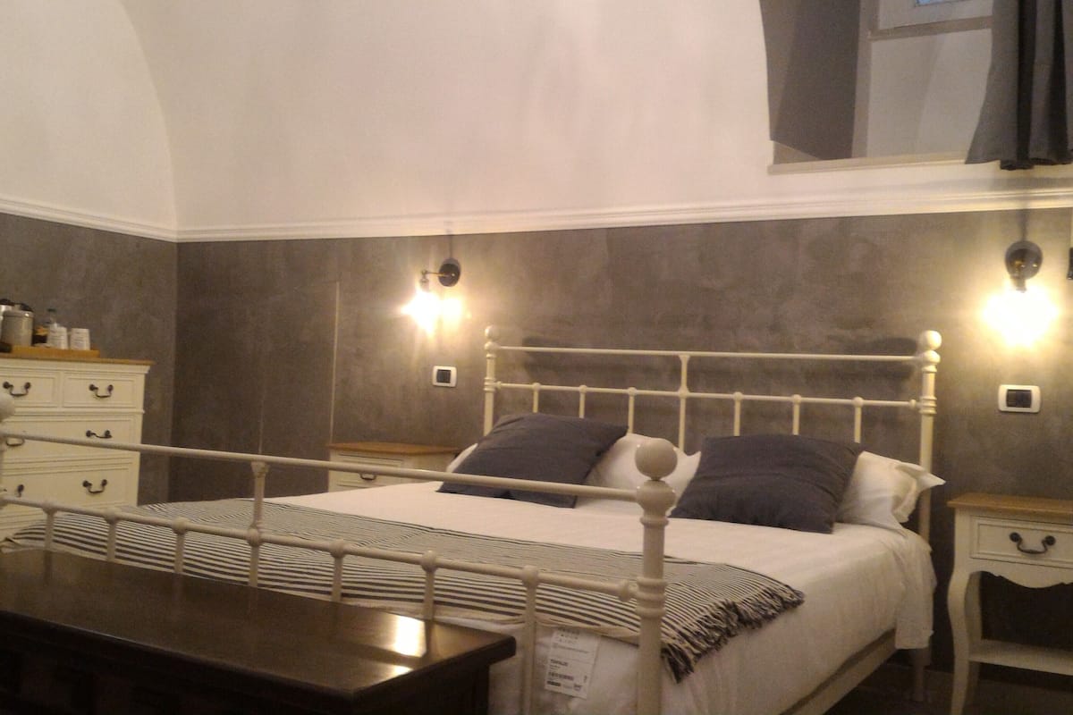 A bedroom with a four-poster bed, bedside tables, a dresser, and wall-mounted lights.