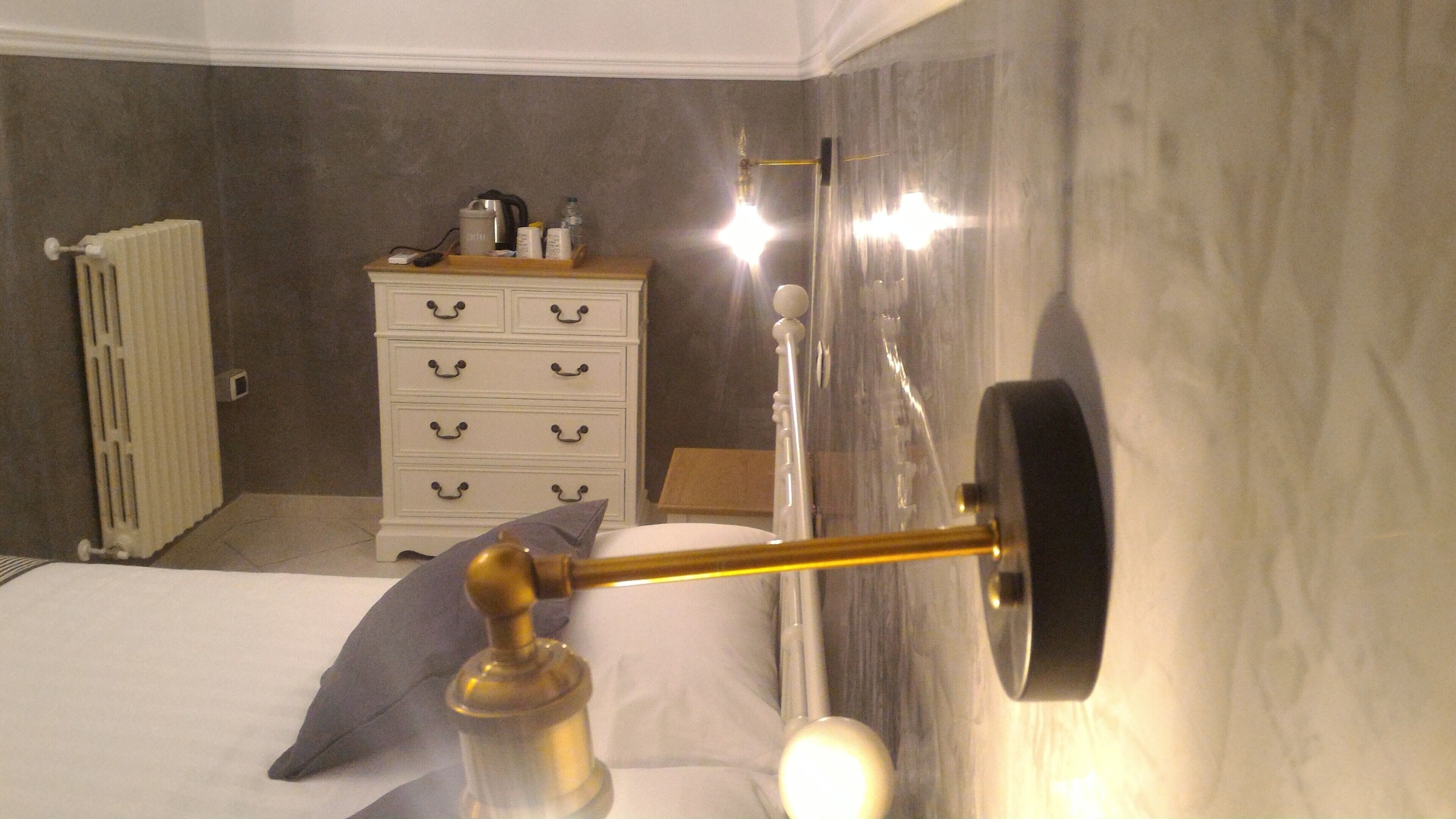 A bathroom with a bed, a white dresser, a radiator, and a shower curtain rod.