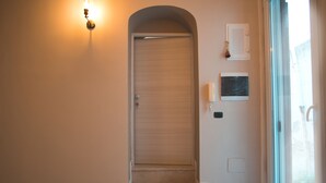 A hallway with a closed door, a wall-mounted light fixture, a small framed picture, and a window with a view of the outdoors. - IL VICOLO (Ruvo di Puglia)