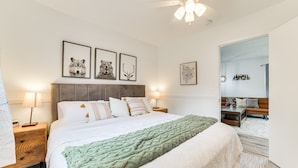 Une chambre à coucher avec un lit, des tables de chevet, un ventilateur de plafond et des tableaux encadrés accrochés au mur.