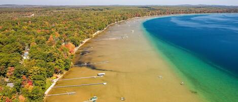 An aerial view of a coastal area with a clear beach, boats, and a forested shoreline.