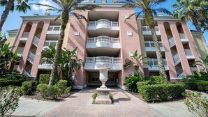 Un hotel de varios pisos con balcones, palmeras y una fuente central.