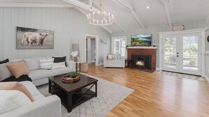 A spacious living room with a high ceiling, a fireplace, and a large TV. - Luxury Riverfront Escape- Hot tub & Fire Pit (Roseburg)