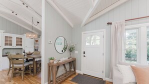 A cozy room with a wooden dining table, chairs, a console table with decorative items, a large mirror, and a white door with a window. - Luxury Riverfront Escape- Hot tub & Fire Pit (Roseburg)