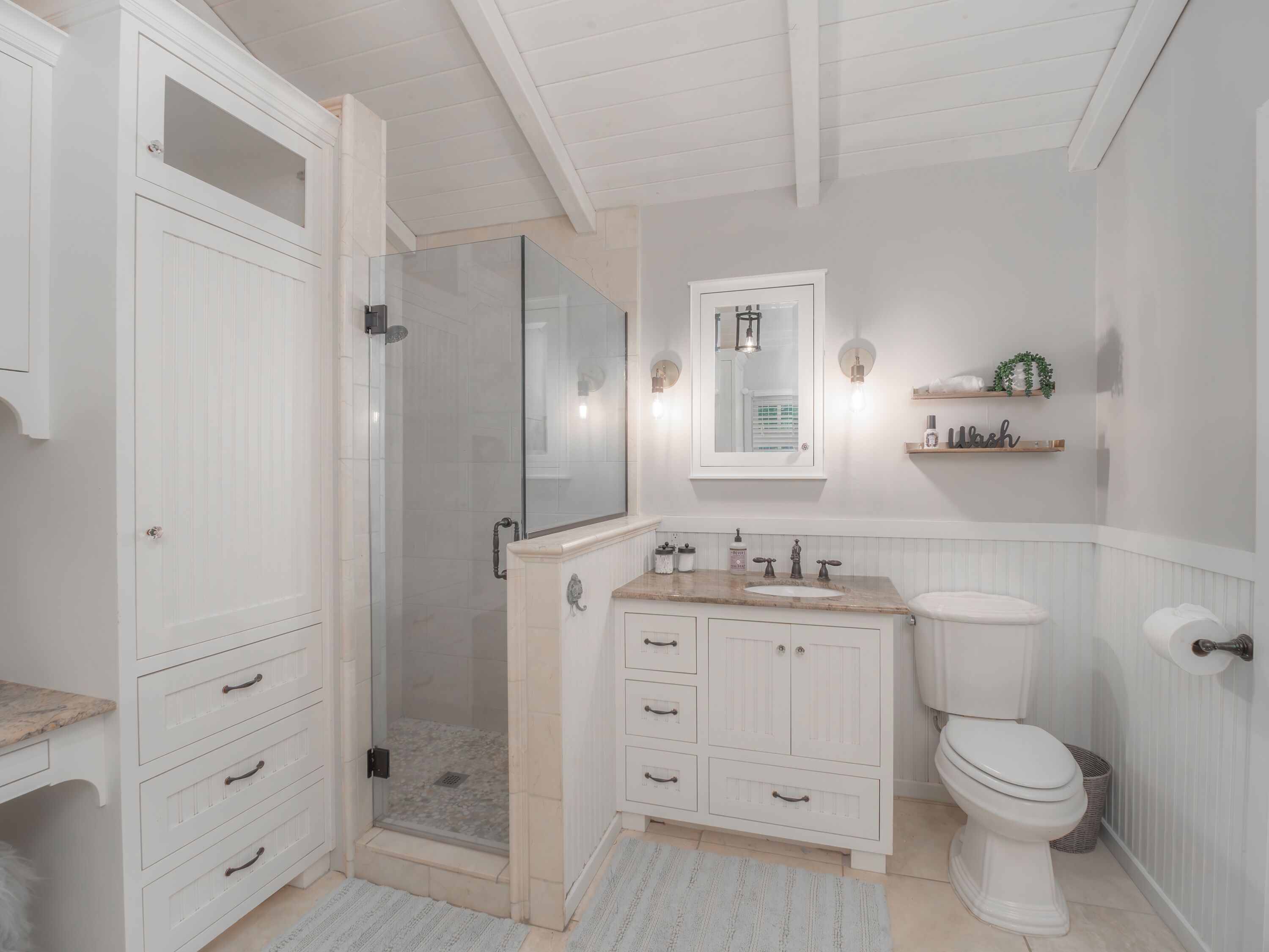 A bathroom with a walk-in shower, a toilet, a sink, and a vanity with drawers.