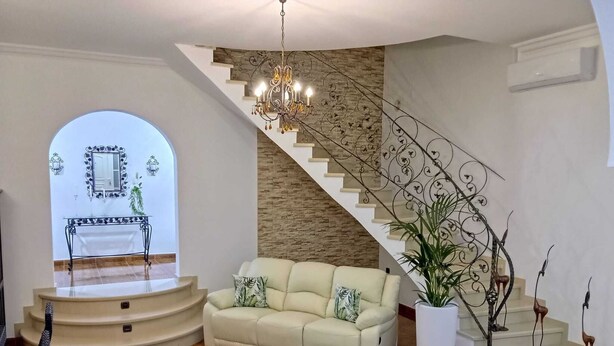 Ein geräumiger Wohnbereich mit einem beigefarbenen Sofa, einem runden Couchtisch und einer Treppe mit einer dekorativen Geländer.