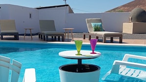 Ein Poolbereich mit Liegestühlen, einem Tisch mit bunten Gläsern und einem weißen Gebäude im Hintergrund.