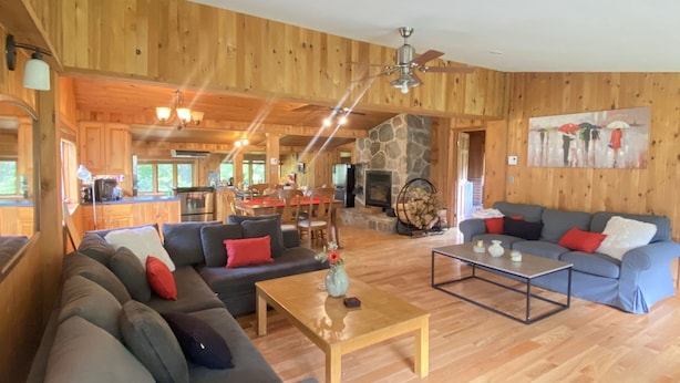 A spacious living area with a large sofa, a coffee table, and a fireplace. - Superbe Chalet au Coeur de la Nature et à Proximité D'un Corridor Aérobique (Montcalm)