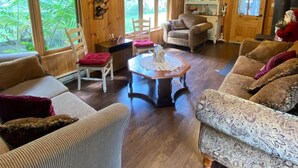 A cozy cabin interior with wooden walls and floors, a dining area with a table and chairs, and a large window offering a view of greenery outside. - Superbe Chalet au Coeur de la Nature et à Proximité D'un Corridor Aérobique (Montcalm)