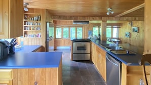 A wooden cabin kitchen with a central island, built-in shelves, and a large window. - Superbe Chalet au Coeur de la Nature et à Proximité D'un Corridor Aérobique (Montcalm)