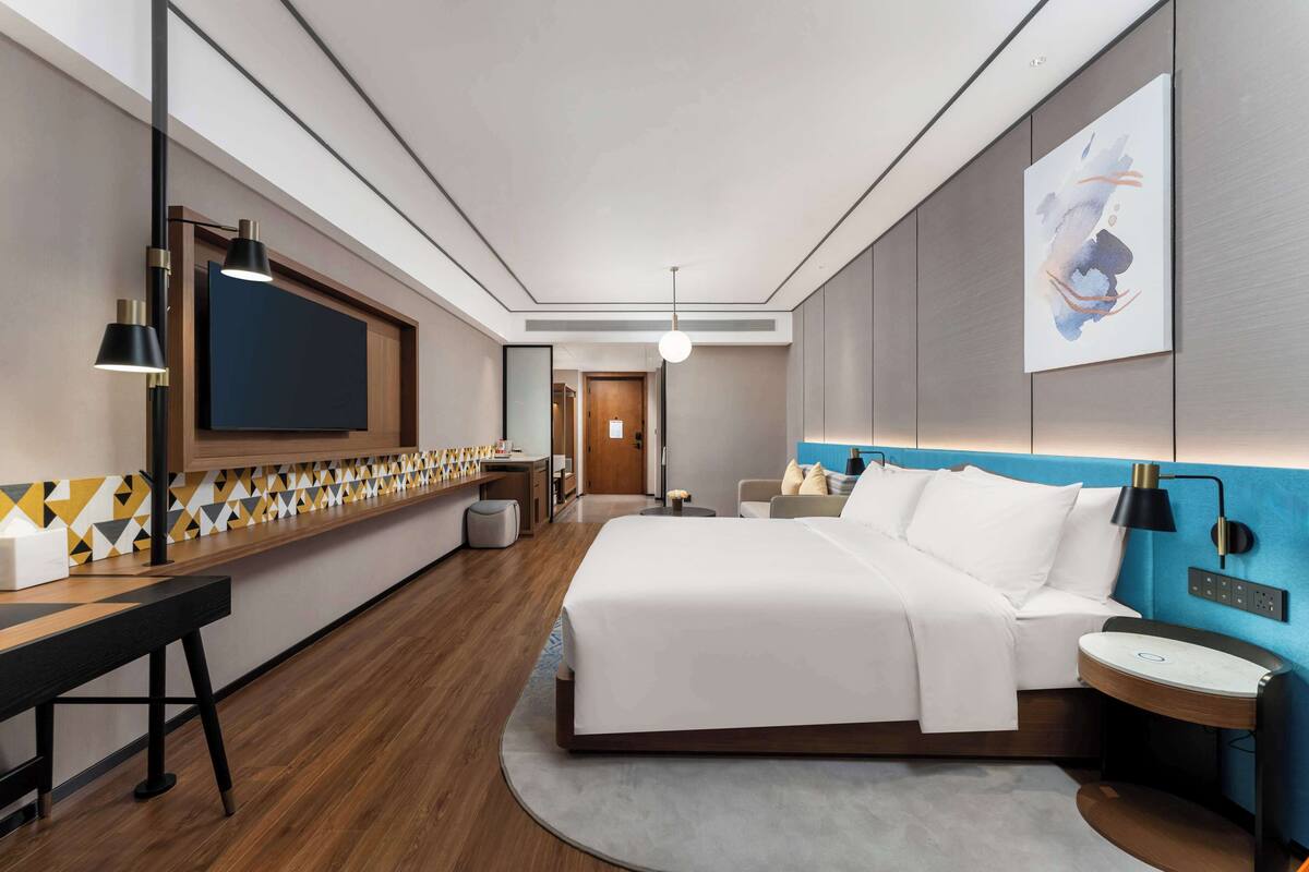 Una habitación de hotel moderna con una cama grande, un escritorio con televisión de pantalla plana, una mesita de noche y una obra de arte colgada en la pared.