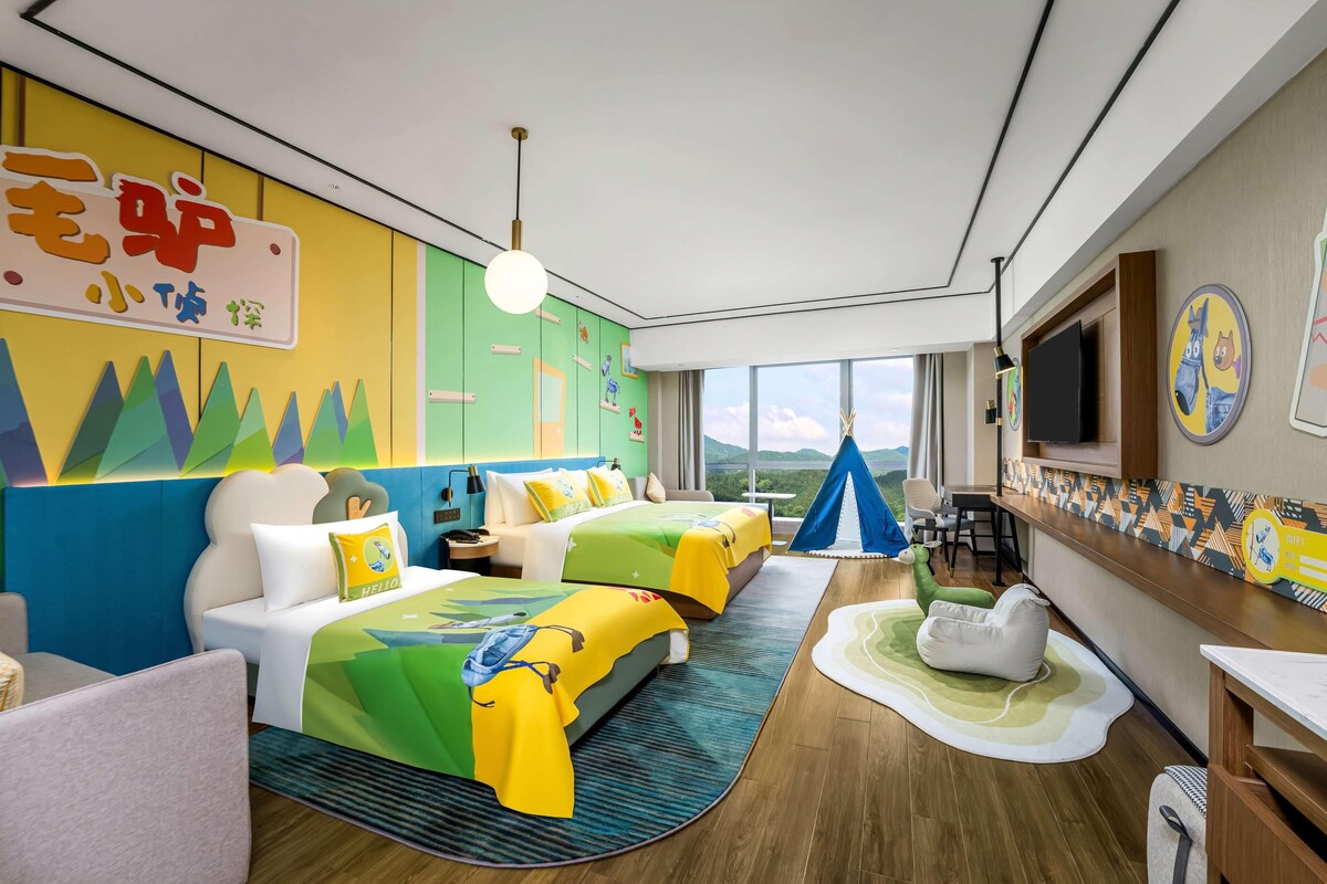 Ein Hotelzimmer mit zwei Betten, einem Fernseher, einem Schreibtisch und einem großen Fenster mit Blick.