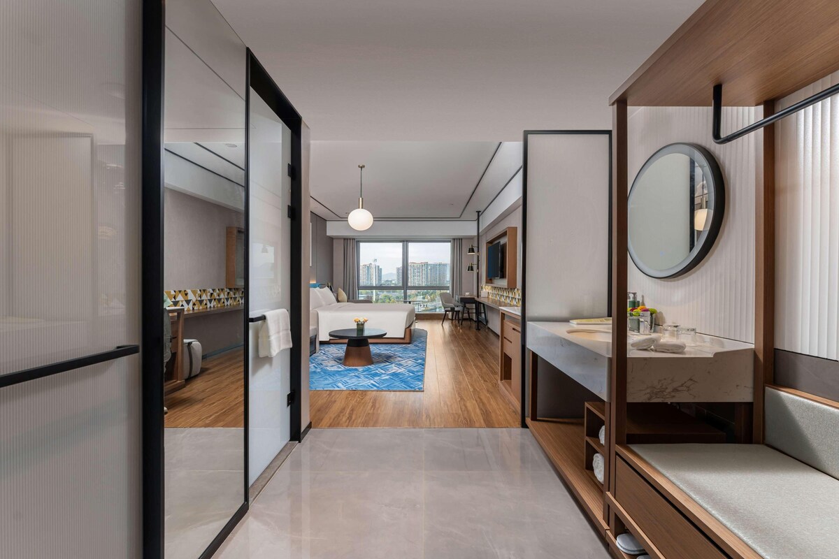 Une chambre d’hôtel moderne dotée d’un grand lit, d’un coin salon avec une table basse, d’une salle de bain avec un miroir et un lavabo, et offrant une vue sur la ville.