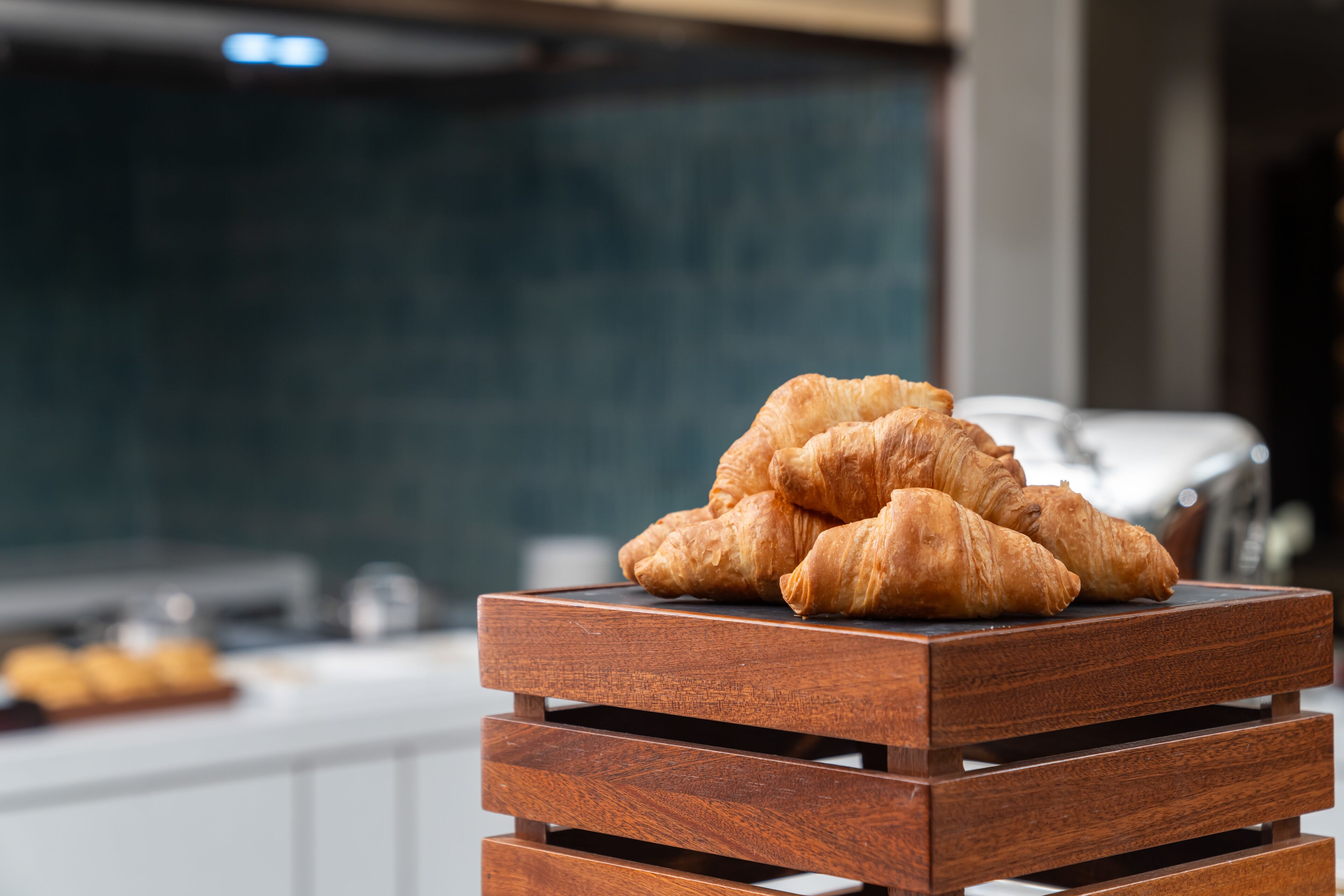 Eine Stapel Croissants auf einem hölzernen Präsentierteller in einer Küche.