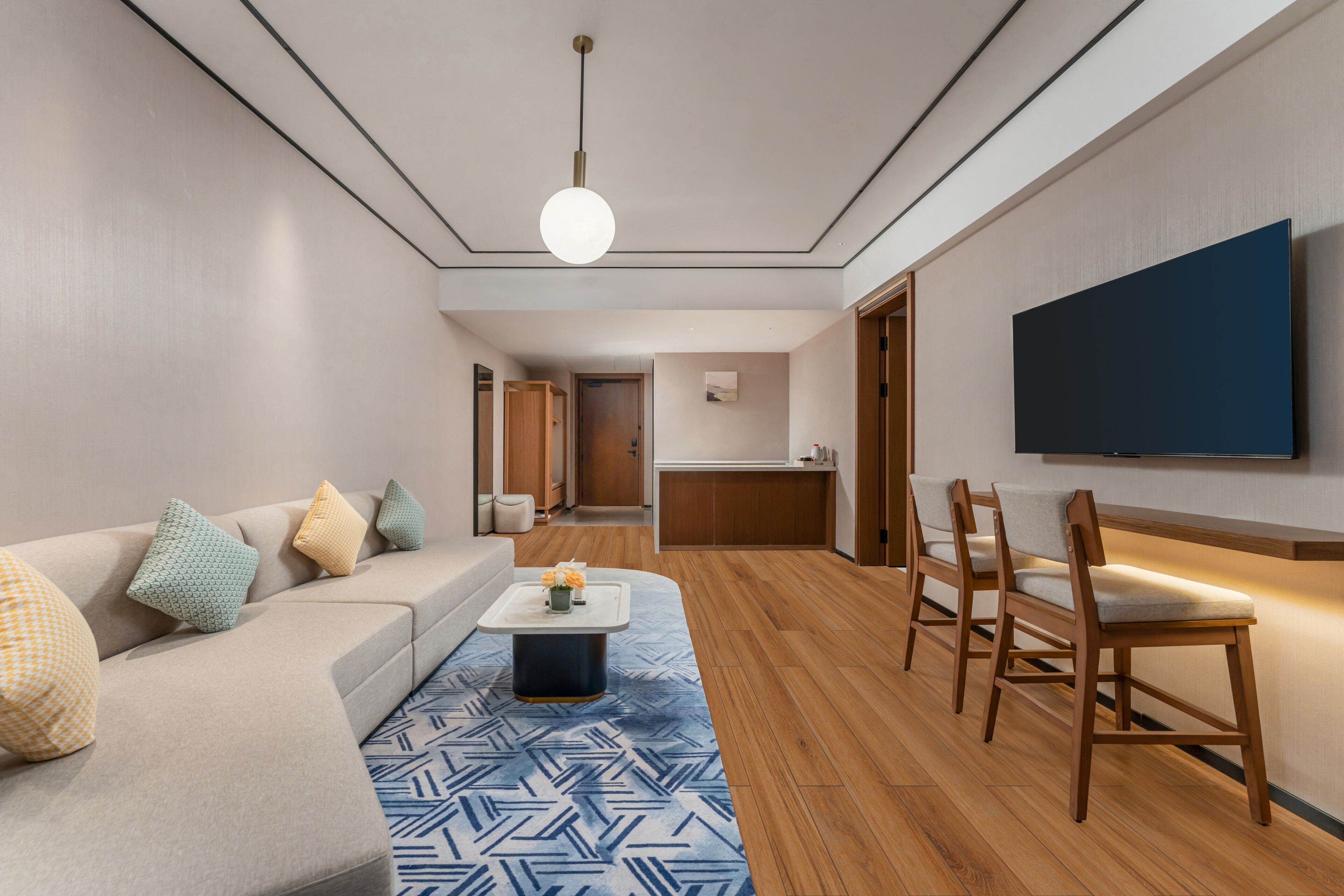 Ein modernes Wohnzimmer mit einer Couch, Sesseln, einem Couchtisch und einem an der Wand befestigten Fernseher.