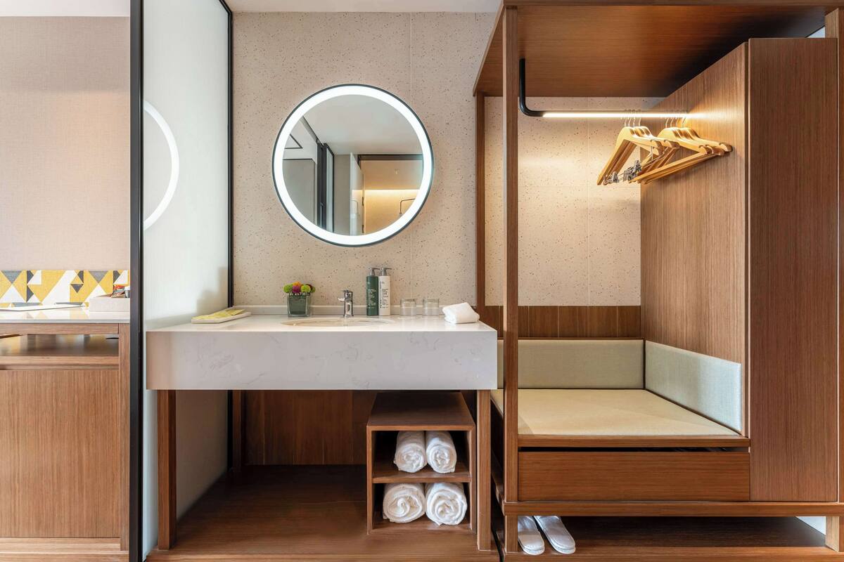 Un baño moderno con tocador de madera, un espejo redondo, un banco empotrado y un perchero para toallas.
