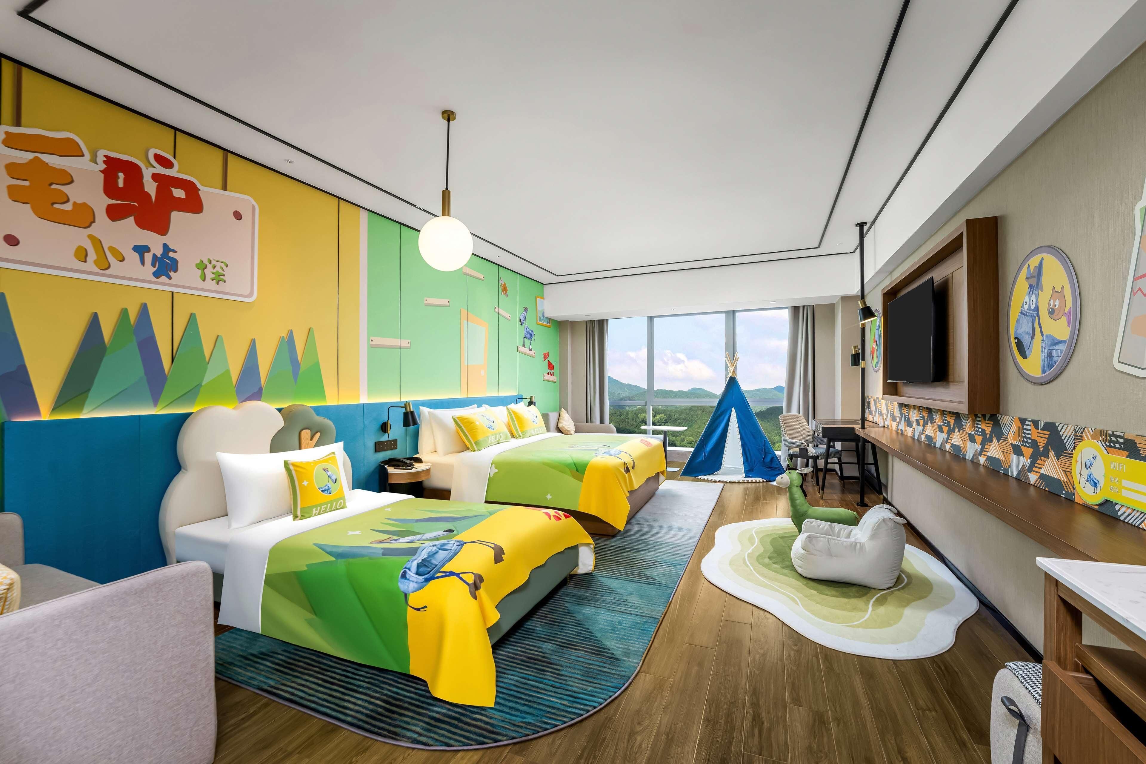 Habitación de hotel con dos camas, televisión, escritorio y un amplio ventanal con vistas.